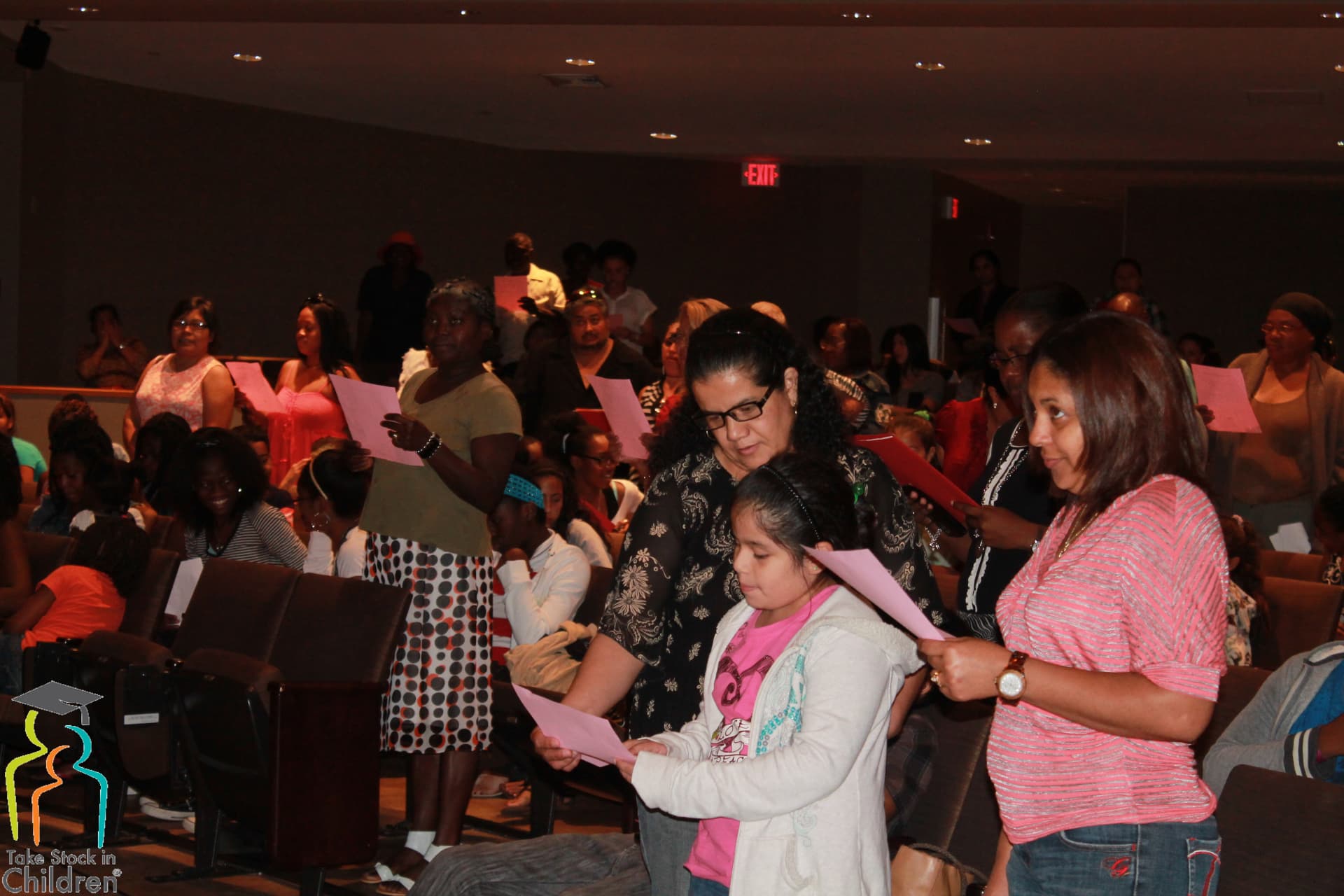 Families and students standing in a Miami Dade College auditorium holding registration slips.