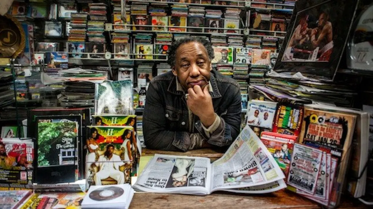 Earl Moodie behind the counter at Moodies Records, surrounded by records, magazines and newspapers.