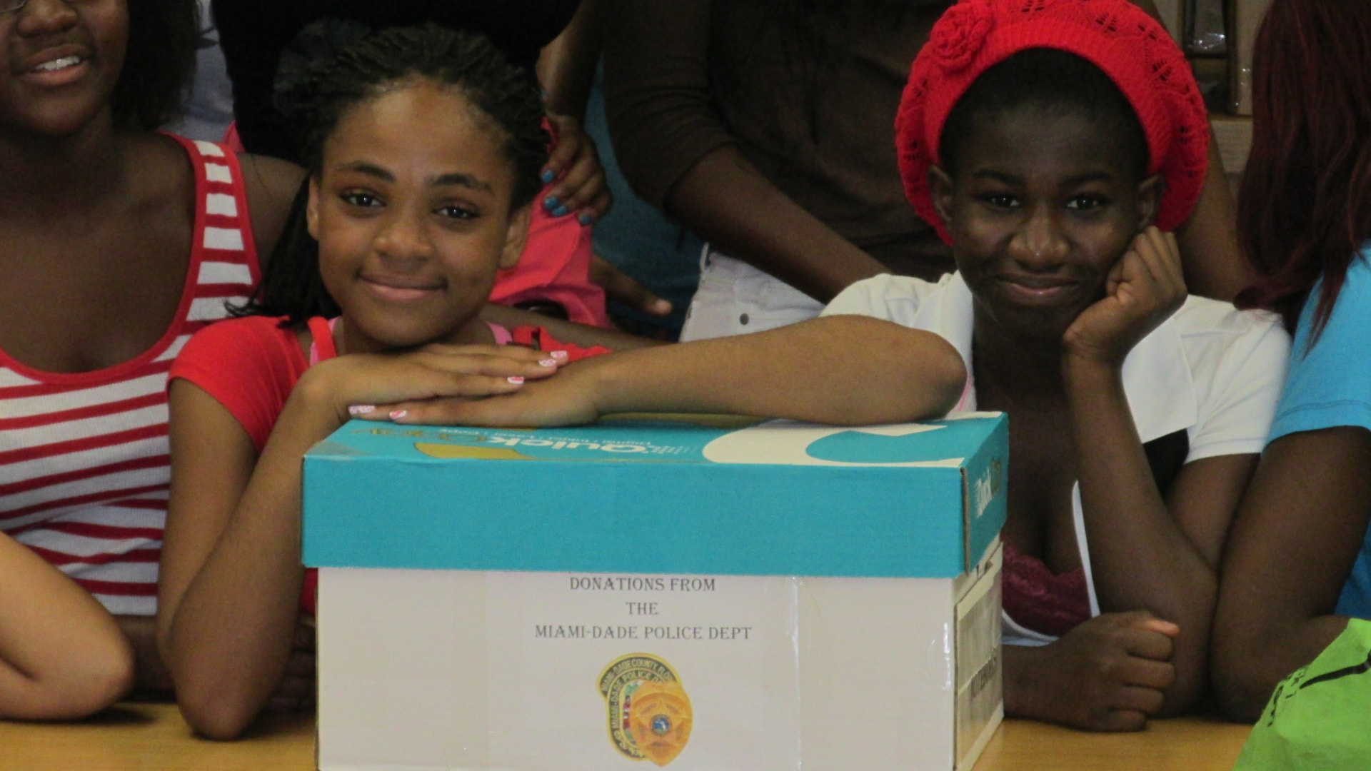 Two students resting on a donation box labeled “Donations from the Miami-Dade Police Dept.”
