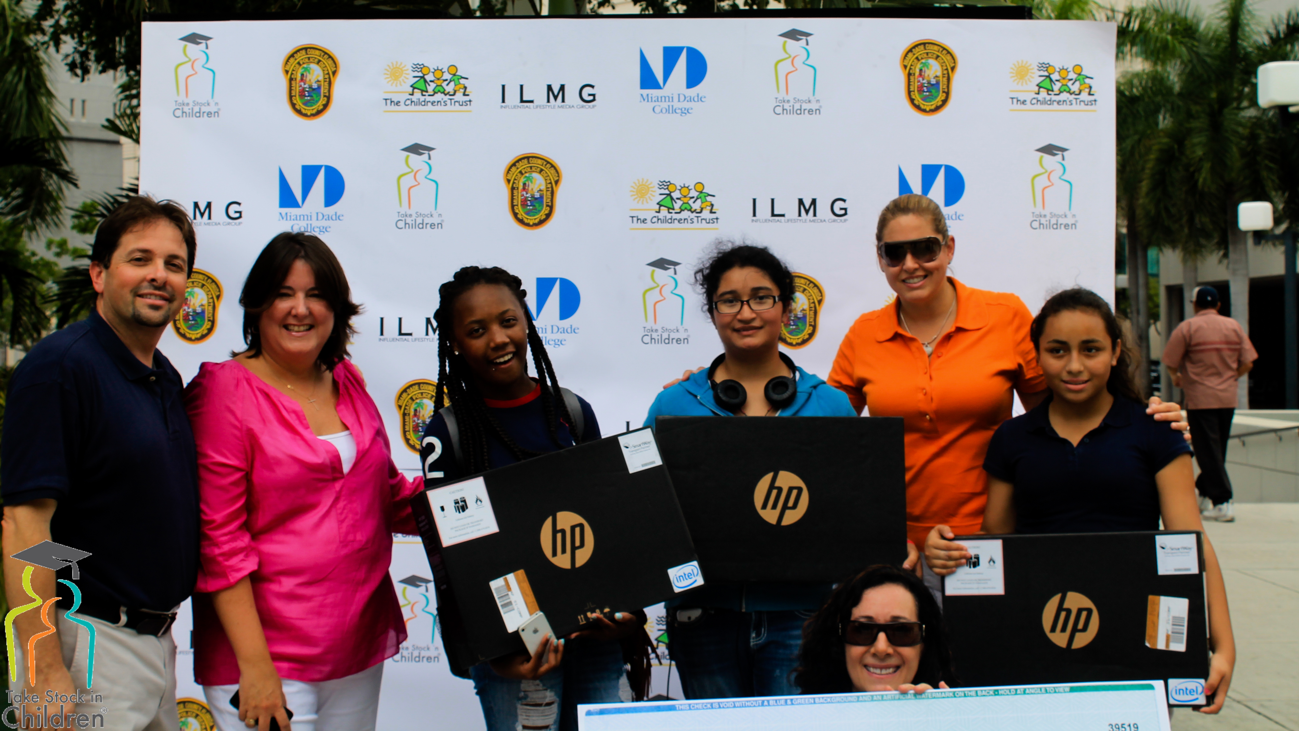 Students hold donated HP laptops in front of the Take Stock in Children, The Children's Trust, ILMG, and Miami-Dade College partner backdrop.