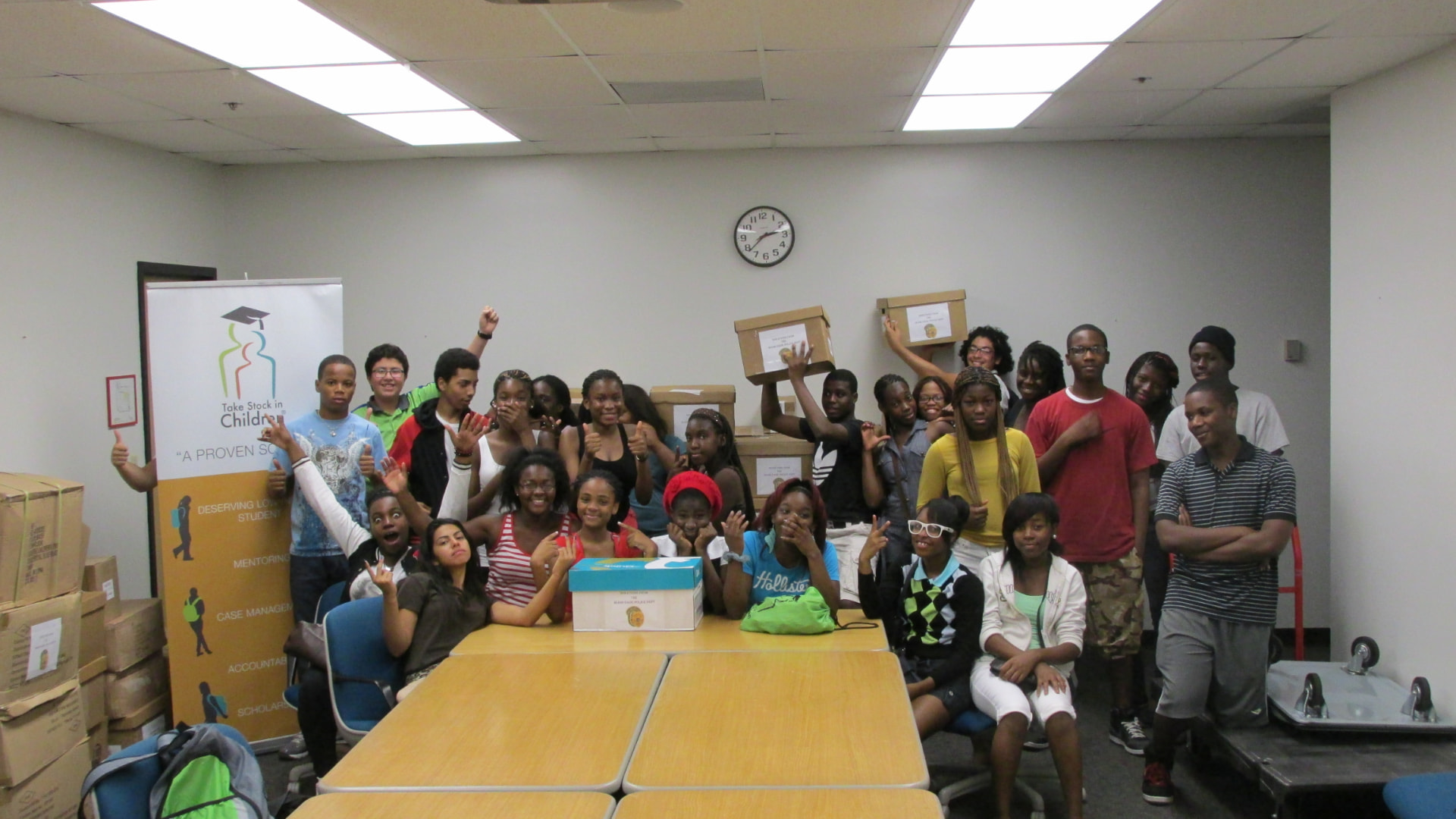 Students gathered in a Take Stock in Children room with donated school supplies stacked in boxes.