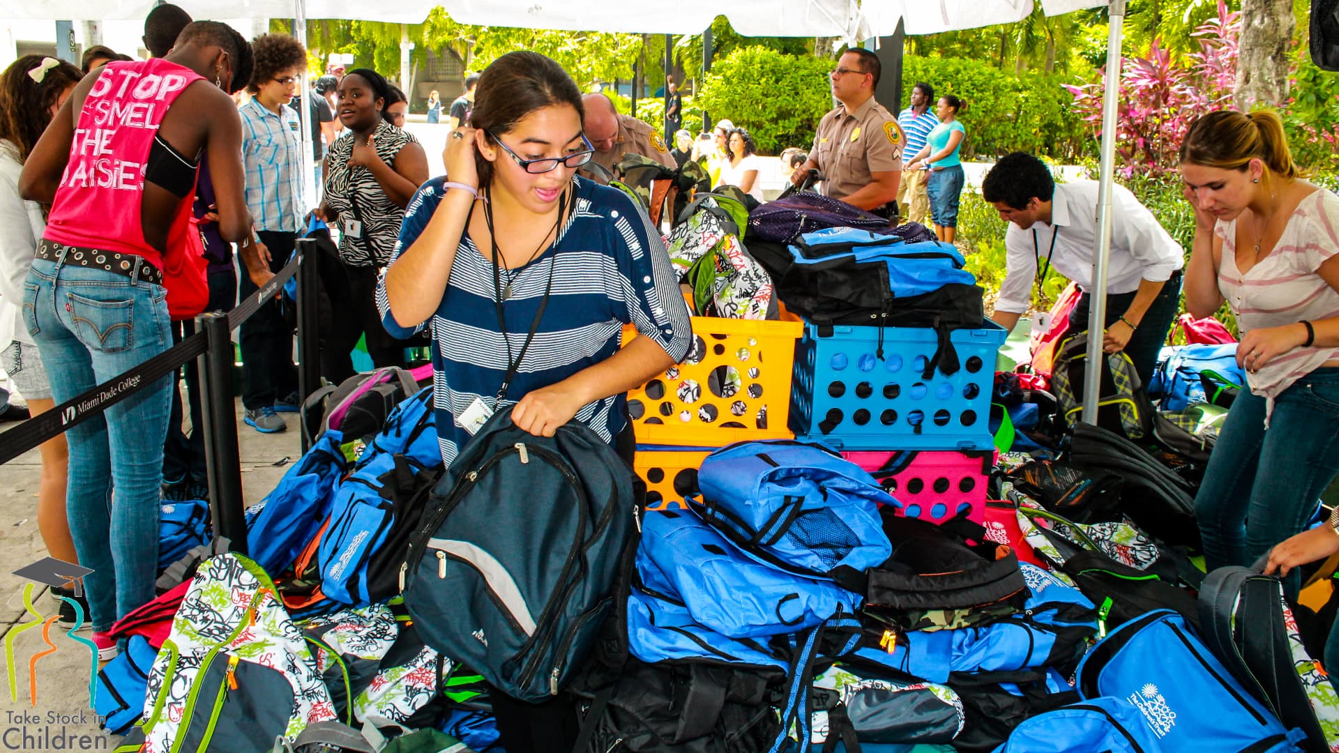 A student selecting a backpack from tables stacked with donated backpacks under a tent.