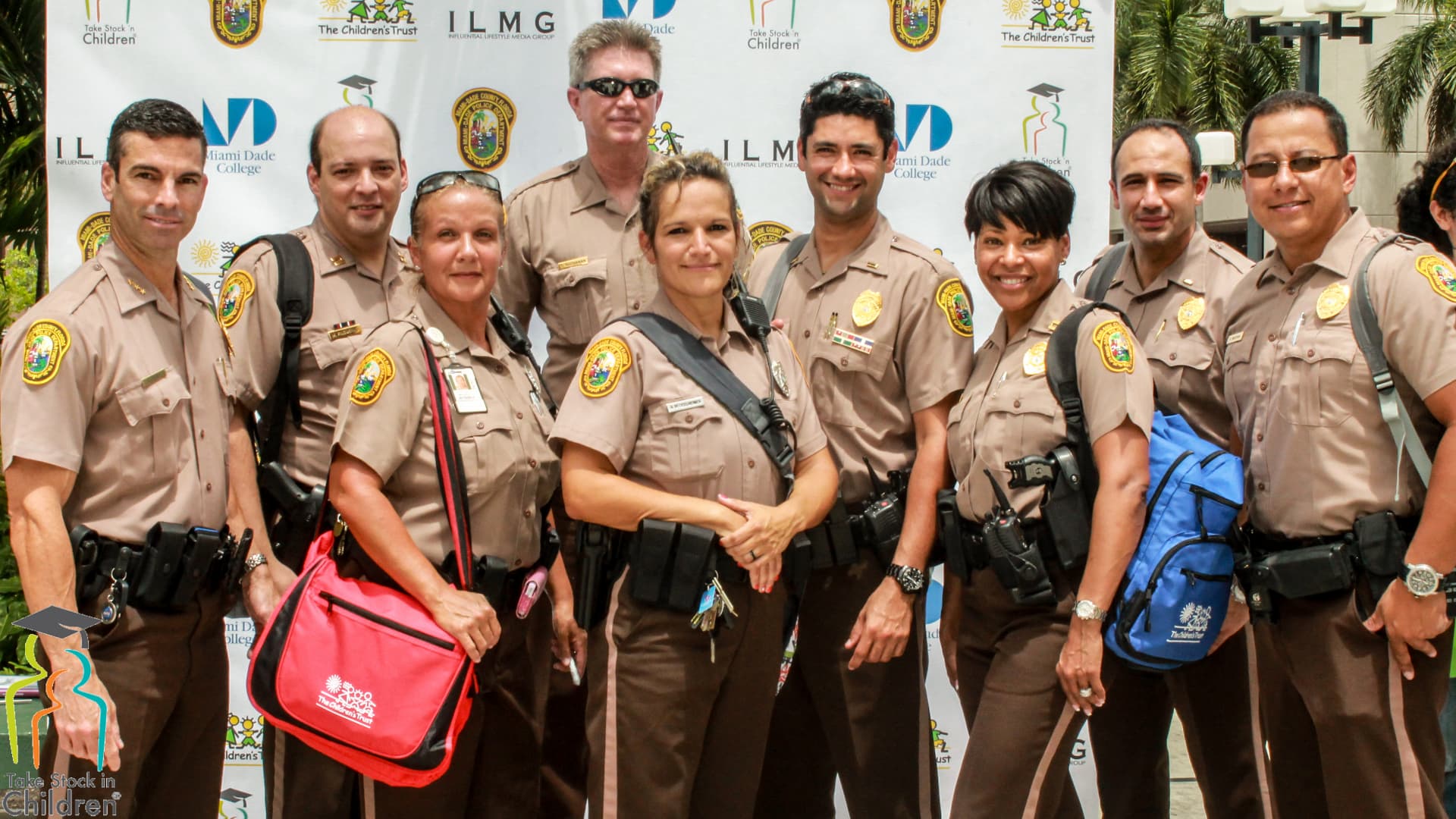 Miami-Dade Police Department officers photographed in front of the Take Stock in Children, The Children's Trust, ILMG and Miami Dade College partner backdrop.