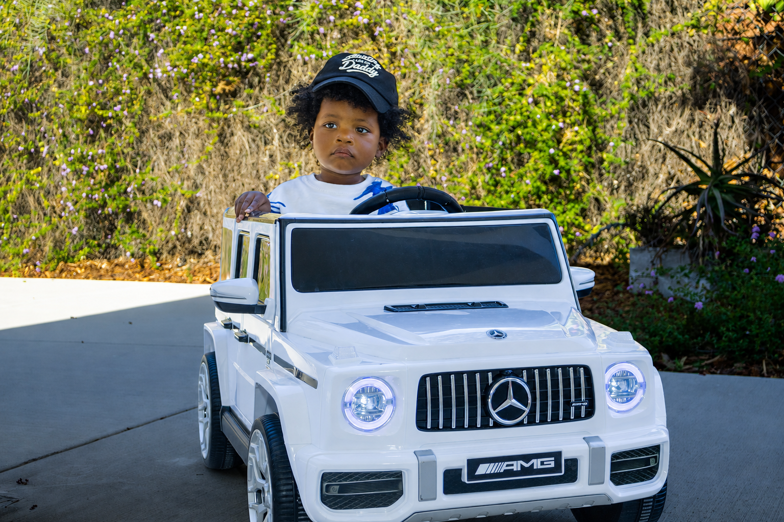 Child wearing a cap in a white toy car for Legacy Team