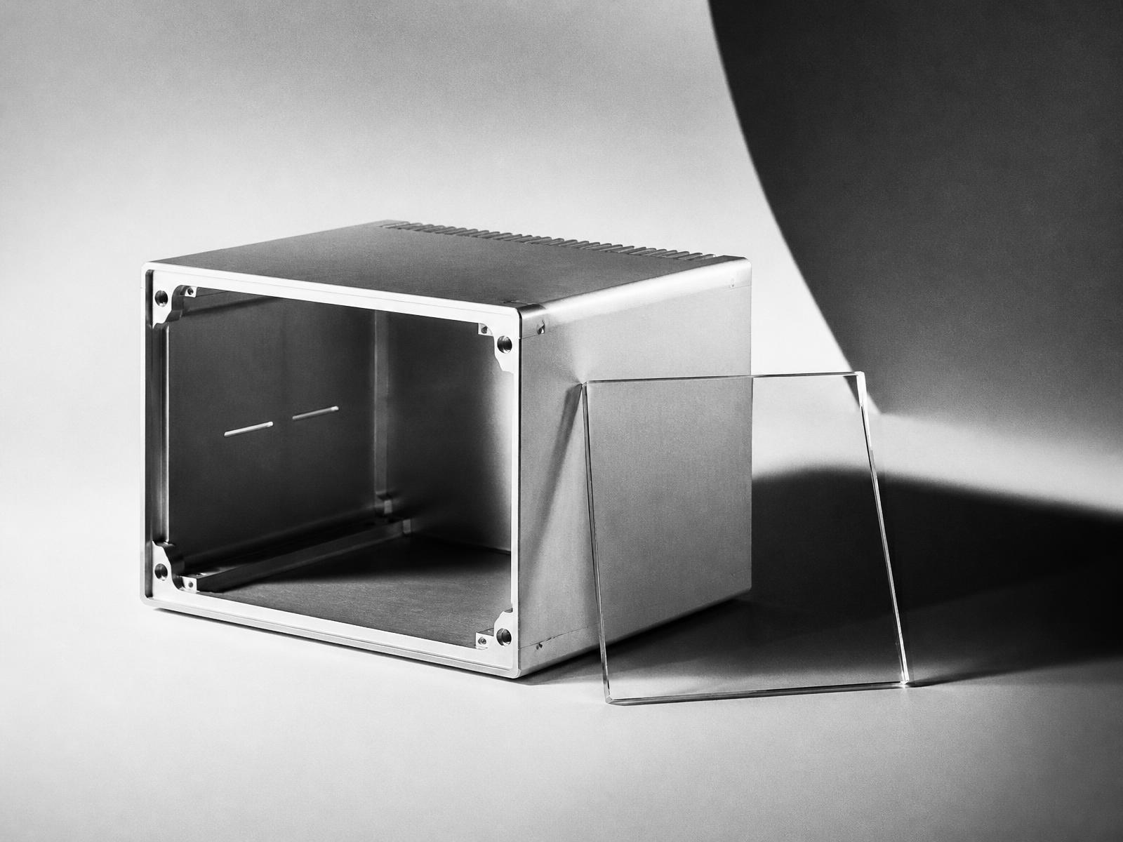 A machined metal enclosure and glass panel photographed as a product study